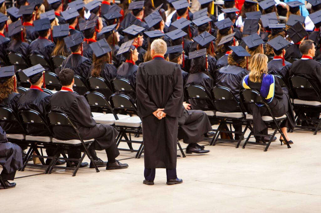 A school master watching over a crowd of graduate students.