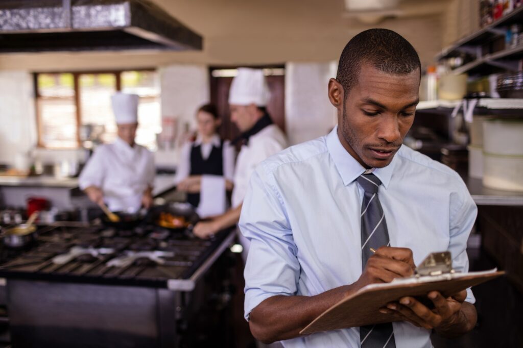 Male manager writing on a clipbaord in kitchen at hotel