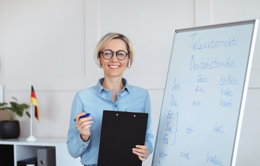 Online schooling. Positive German teacher posing near blackboard with grammar rules, looking at