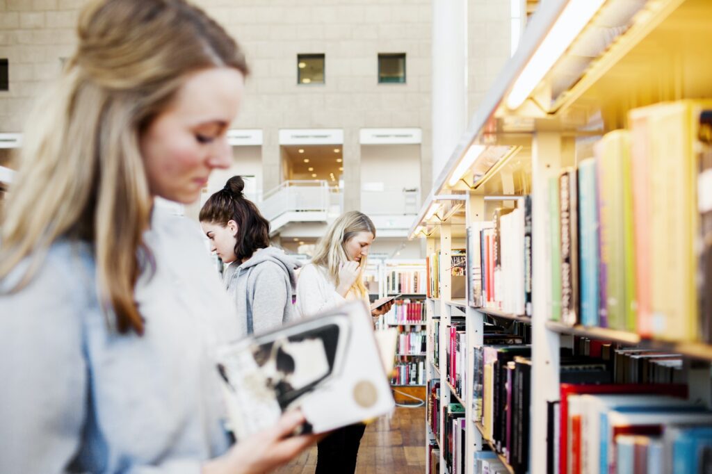 Female university students choosing books in library